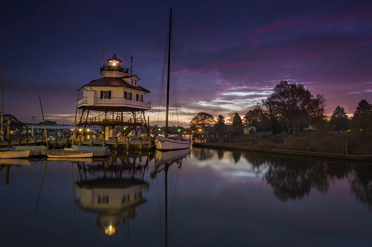 Drum Point Lighthouse on its screwpile legs at sunrise, lit against a violet sky and mirrored in the water at Solomons.